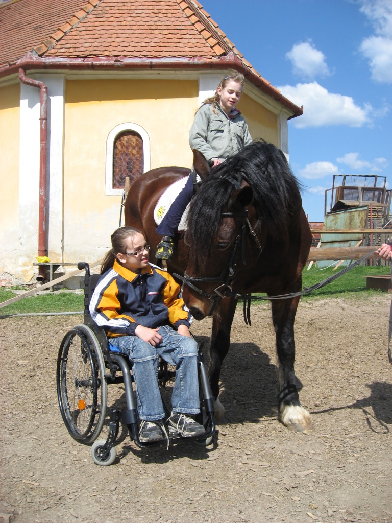 Dievča na vozíku pri koni s druhým dieťaťom v sedle